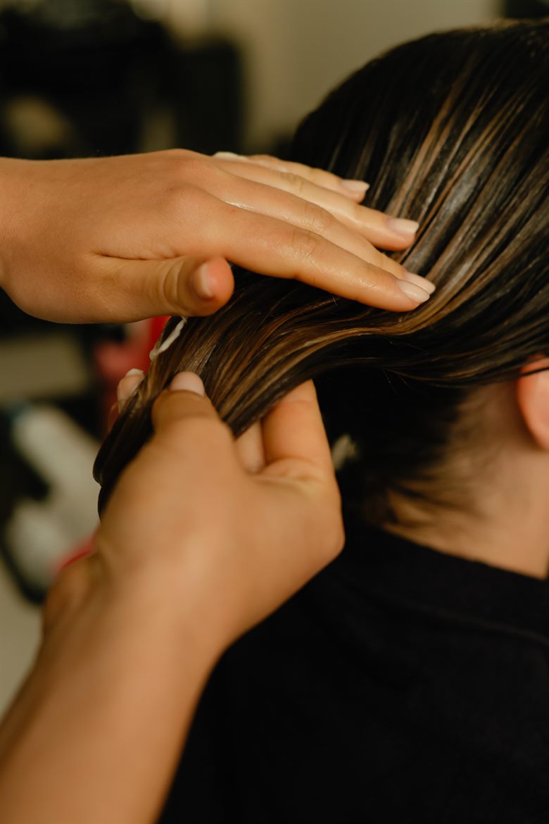 A stylist’s hands working refreshed colour and dimension through mid-lengths.